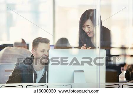 Stock Image - University students working at computer behind glass partition. Fotosearch