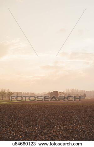 Stock Image - View of ploughed fields and distant farm buildings in mist. Fotosearch
