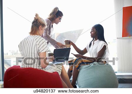 Woman handing takeaway coffee to businesswomen sitting on beanbags View Large Photo Image Stock Photo - Woman handing takeaway coffee to businesswomen sitting on beanbags. Fotosearch