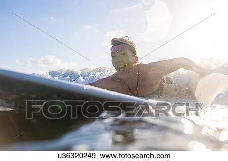 Stock Photo - Woman having fun paddling on surfboard in sea, Nosara, Guanacaste Province, Costa Rica. Fotosearch