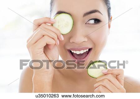 Stock Image - Woman holding cucumber in front of eye. Fotosearch