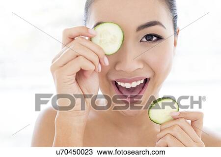 Stock Image - Woman holding cucumber in front of eye. Fotosearch