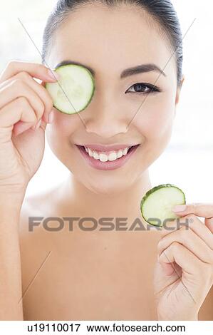 Stock Photo - Woman holding cucumber in front of eye. Fotosearch