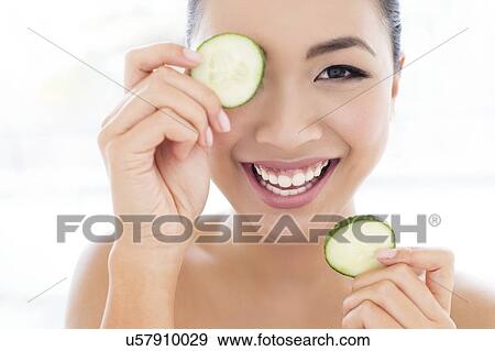 Stock Photo - Woman holding cucumber in front of eye. Fotosearch