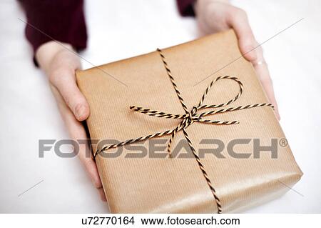 Woman holding gift wrapped in brown paper, decorated with string, close-up View Large Photo Image Picture - Woman holding gift wrapped in brown paper, decorated with string, close-up. Fotosearch