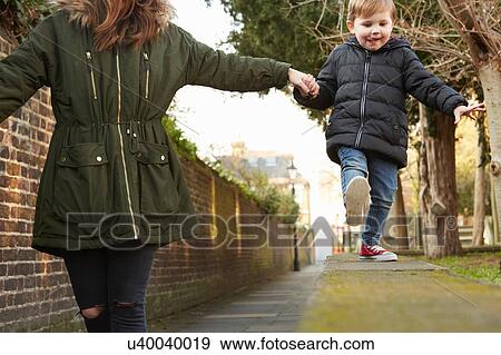 Stock Photo - Woman holding toddler son's hand walking on street wall. Fotosearch