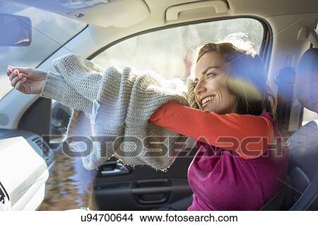 Picture - Woman in car taking off sweater. Fotosearch