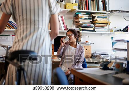 Woman in office drinking coffee chatting to colleague View Large Photo Image Stock Photo - Woman in office drinking coffee chatting to colleague. Fotosearch