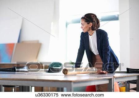 Stock Photography - Woman in office leaning against desk looking away. Fotosearch