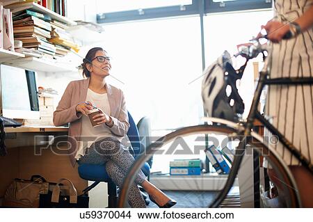Picture - Woman in office with coffee chatting to colleague. Fotosearch
