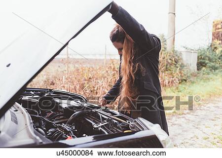 Picture - Woman looking at car engine on roadside. Fotosearch