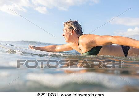 Stock Image - Woman paddling on surfboard in calm sea, Nosara, Guanacaste Province, Costa Rica. Fotosearch