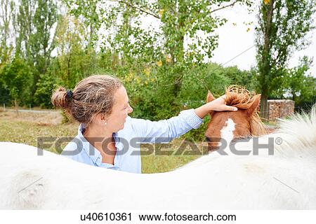 Stock Image - Woman petting horse's forelock in field. Fotosearch