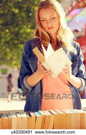 Stock Image - Woman reading at book stall, London, UK. Fotosearch
