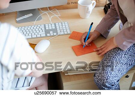 Stock Photo - Woman sitting on desk writing on notepad. Fotosearch