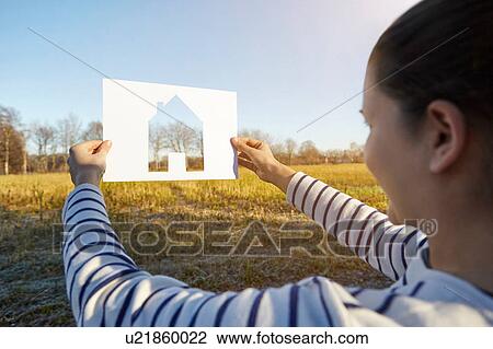 Woman standing in rural setting, holding out paper with cut-out of house View Large Photo Image Stock Image - Woman standing in rural setting, holding out paper with cut-out of house. Fotosearch