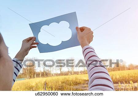 Woman standing in rural setting, holding paper with cut-out of cloud, towards sky View Large Photo Image Stock Image - Woman standing in rural setting, holding paper with cut-out of cloud, towards sky. Fotosearch