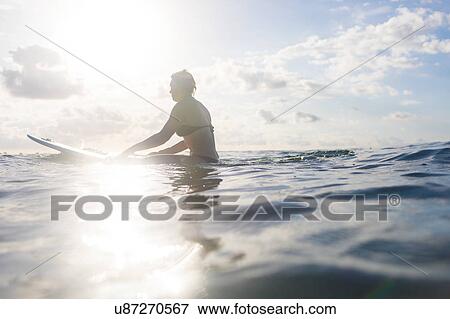 Stock Photo - Woman straddling surfboard in sunlit sea, Nosara, Guanacaste Province, Costa Rica. Fotosearch