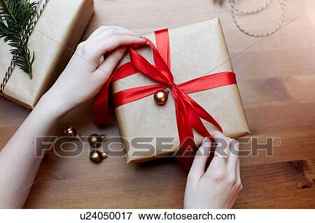 Woman tying red bow on Christmas gift, overhead view View Large Photo Image Stock Photo - Woman tying red bow on Christmas gift, overhead view. Fotosearch
