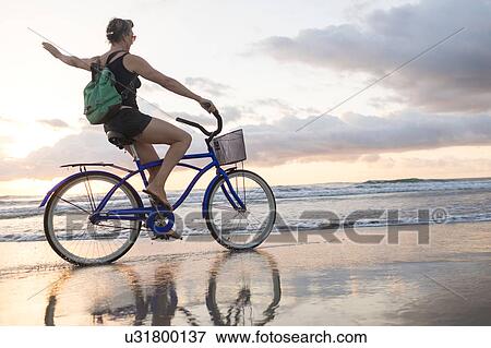 Woman waving while cycling on beach at sunset, Nosara, Guanacaste Province, Costa Rica View Large Photo Image Stock Photo - Woman waving while cycling on beach at sunset, Nosara, Guanacaste Province, Costa Rica. Fotosearch