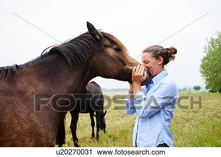 Stock Image - Woman with her face to horse's muzzle in field. Fotosearch
