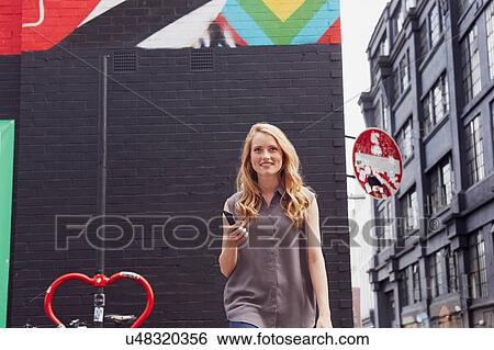 Woman with mobile phone in hand, walking away from wall View Large Photo Image Stock Photograph - Woman with mobile phone in hand, walking away from wall. Fotosearch