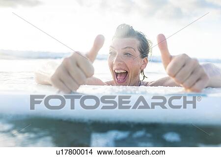 Picture - Woman with surfboard in sea giving thumbs up, Nosara, Guanacaste Province, Costa Rica. Fotosearch