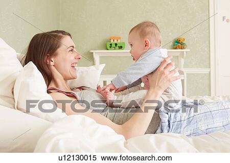 Stock Photography - Women lying on bed playing with baby daughter. Fotosearch
