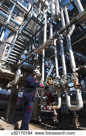 Picture - Worker checking pipework on an oil and gas refinery. Fotosearch
