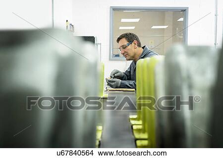 Picture - Worker finishing components in precision casting factory. Fotosearch