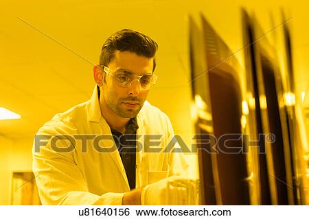 Stock Photograph - Worker inspecting circuit boards in safe yellow light in electronics factory. Fotosearch