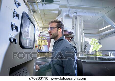 Stock Image - Worker operating ceramic coating plant in precision casting factory. Fotosearch