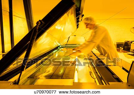 Stock Photo - Worker placing negative of circuit board in machine in safe yellow light in electronics factory. Fotosearch