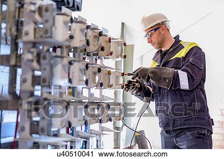 Stock Image - Worker testing circuit breakers in electricity substation. Fotosearch