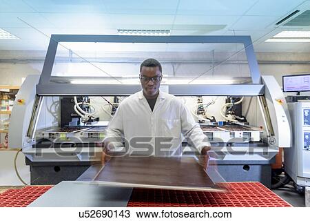 Stock Image - Worker using automated cutting machine to cut circuit boards in electronics factory. Fotosearch