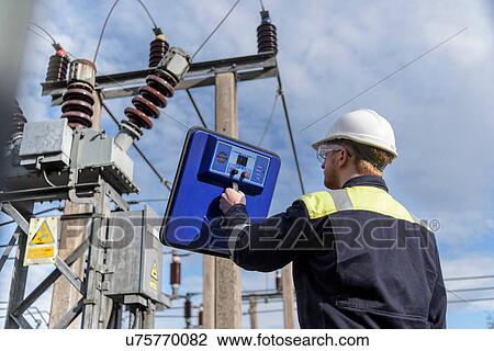 Stock Image - Worker using partial discharge detector in electricity substation. Fotosearch