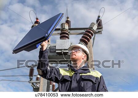 Stock Image - Worker using partial discharge detector in electricity substation. Fotosearch
