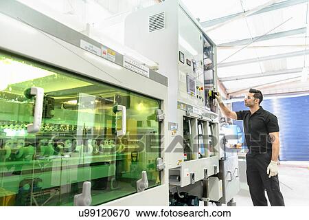 Stock Image - Worker with circuit board processing machine in electronics factory. Fotosearch