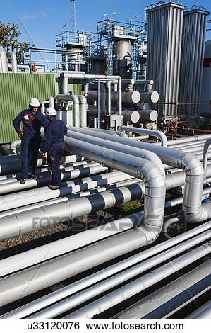 Stock Photograph - Workers checking pipework on an oil and gas refinery. Fotosearch