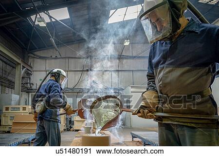 Stock Image - Workers pouring molten aluminium into moulds in precision casting factory. Fotosearch