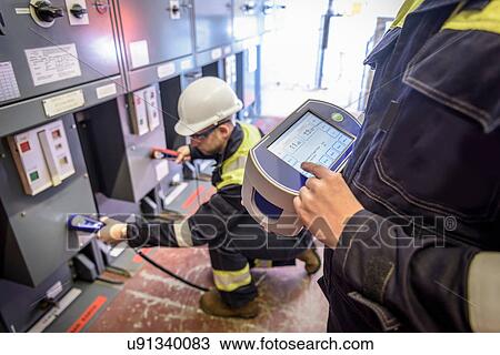 Stock Image - Workers using partial discharge unit in electricity substation. Fotosearch