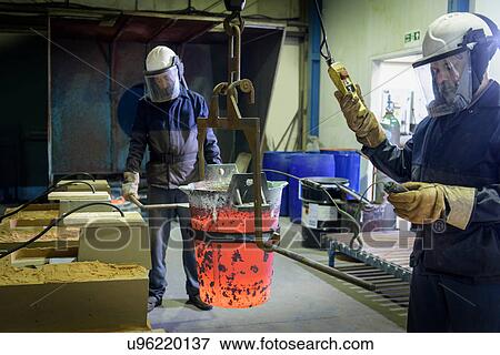 Stock Photo - Workers with molten aluminium alloy flask in precision casting factory. Fotosearch