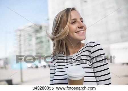 Stock Photography - Young blond haired woman in city with takeaway coffee. Fotosearch