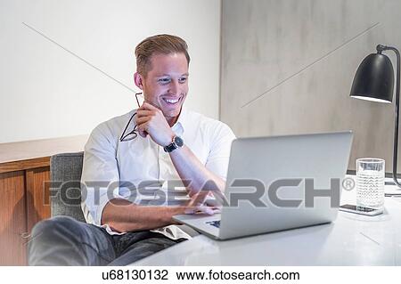 Young businessman at desk looking at laptop View Large Photo Image Stock Image - Young businessman at desk looking at laptop. Fotosearch