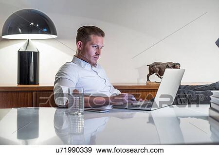 Stock Photo - Young businessman at desk typing on laptop. Fotosearch