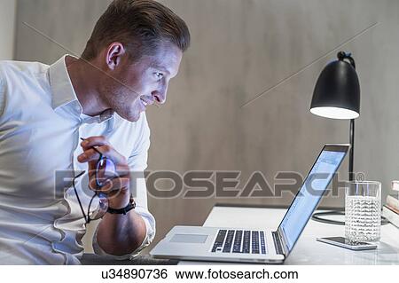Young businessman working late at desk looking at laptop View Large Photo Image Stock Photograph - Young businessman working late at desk looking at laptop. Fotosearch