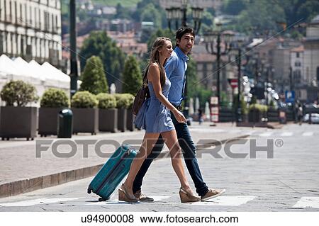 Stock Photo - Young couple crossing road, pulling suitcase, Turin, Piedmont, Italy. Fotosearch