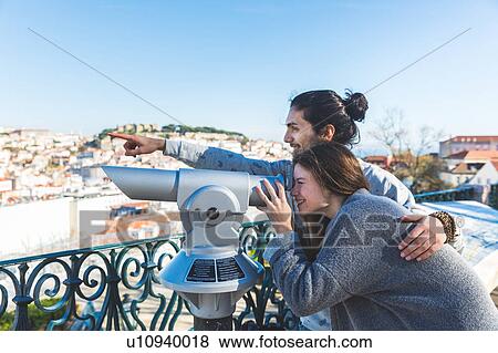 Stock Photo - Young couple, sightseeing, looking through coin operated telescope, Lisbon, Portugal. Fotosearch