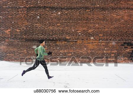 Young female runner in knit hat running along snow covered sidewalk View Large Photo Image Stock Photograph - Young female runner in knit hat running along snow covered sidewalk. Fotosearch