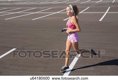 Stock Image - Young female runner running in city parking lot. Fotosearch